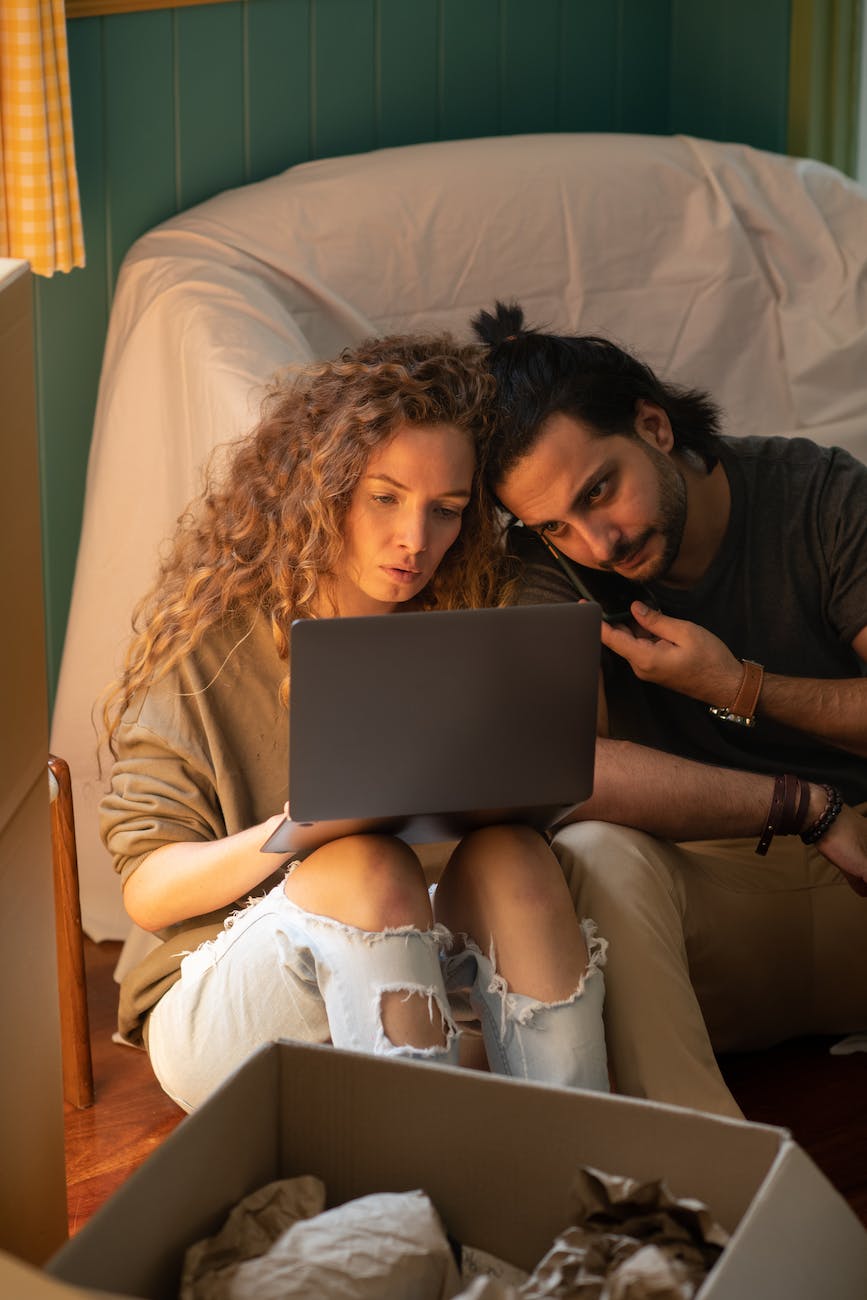 young couple using laptop while sitting on floor in living room