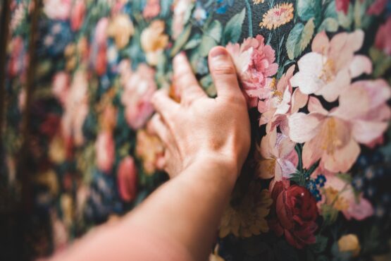 crop person touching colorful floral wallpaper